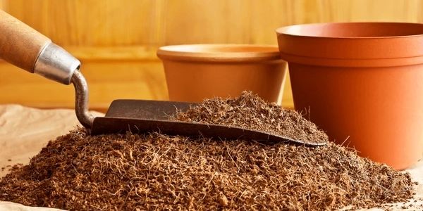 A pile of soil with a gardening trowel and empty plant pots.