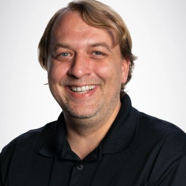 Smiling man in a black polo shirt against a white background.