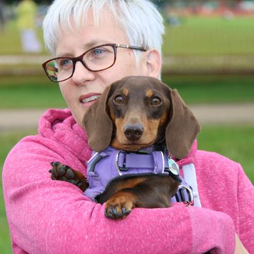 Business owner Clare is holding her chocolate and tan Dachshund in her arms.