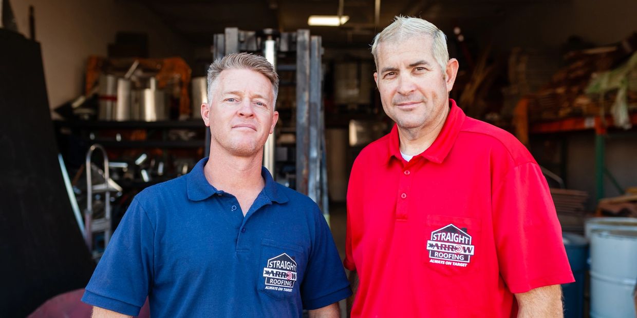 Two men in branded work shirts stand in a workshop.