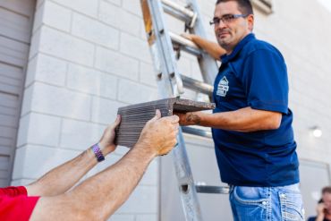 Two men holding a piece of wood near a ladder.