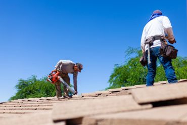 Two workers fixing a roof under a clear blue sky.