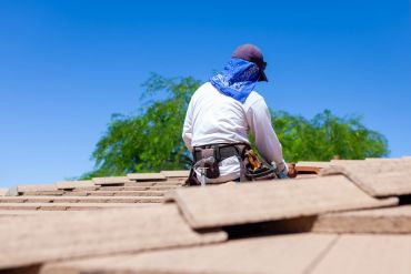 Worker installing roof tiles under clear sky.
