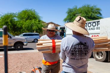 Two workers handling roofing materials outdoors.