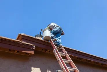 Man on a ladder repairing a roof under clear sky.