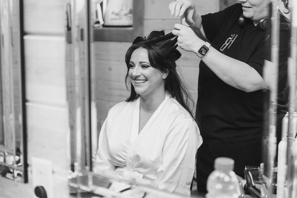 A woman smiling while getting her hair styled by a hairstylist.