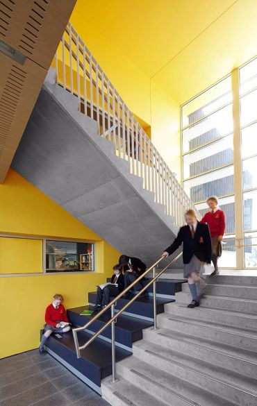 Students in uniforms in a modern yellow stairwell.