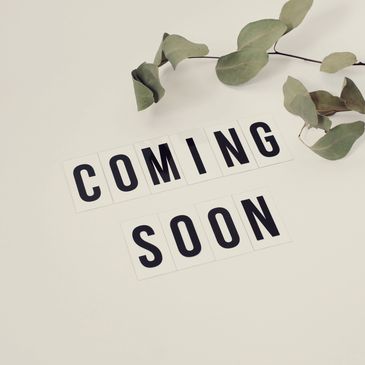 Letter tiles spelling out 'COMING SOON' with green leaves on a white background.