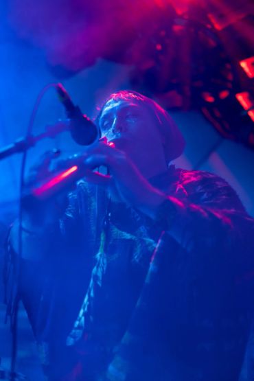 Musician playing flute on stage with blue and red lighting.