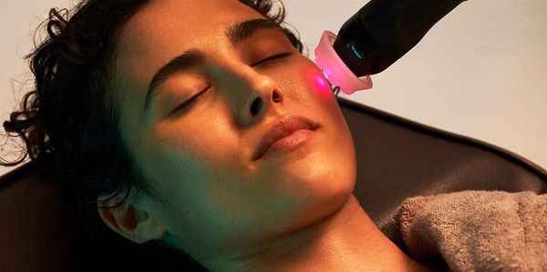 woman's face with a light pink glowing light getting a facial treatment
