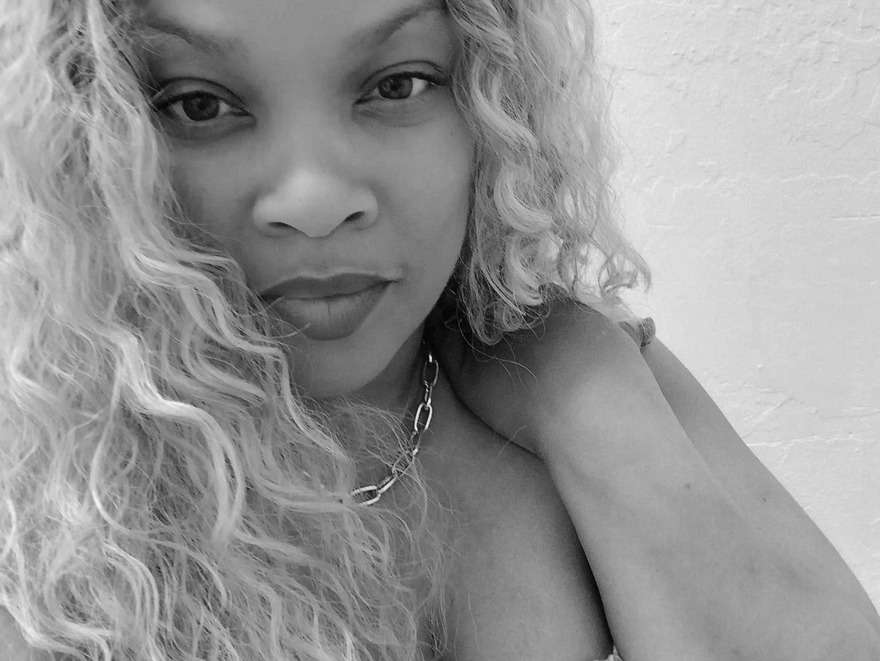 Close-up black and white portrait of a woman with curly hair and a chain necklace.