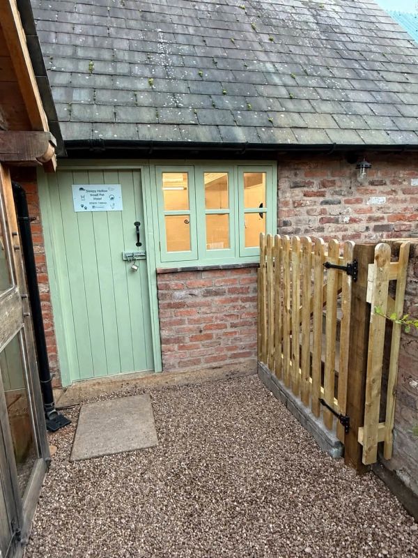 Small brick building with green door and windows and a wooden fence gate.
