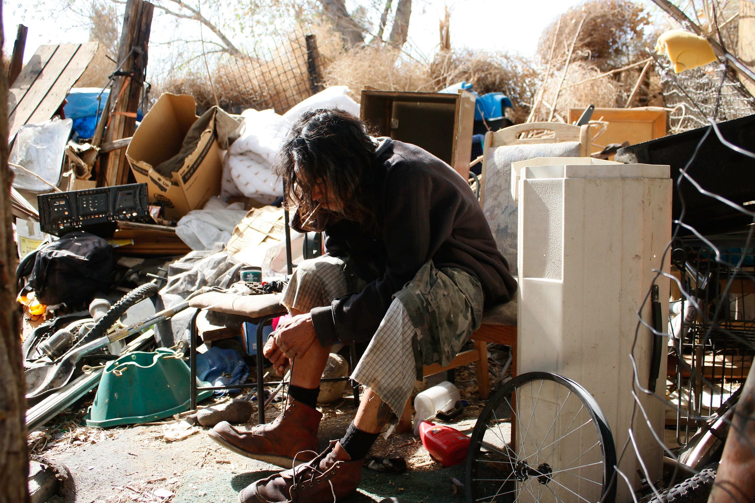 Homeless Native American man ties his shoes in his camp in Apple Valley CA.