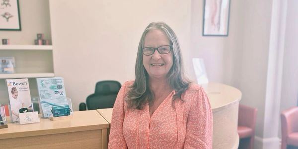 Smiling woman in glasses at a reception desk.