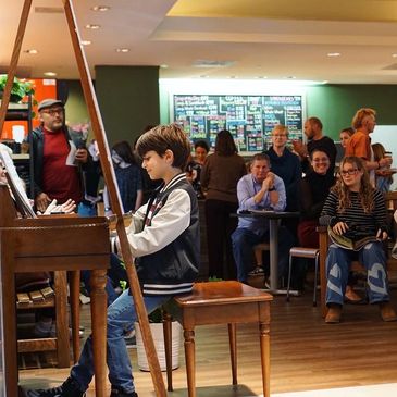 A young boy plays piano for an attentive audience in a cozy venue.