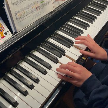 Hands playing piano keys with sheet music in the background.