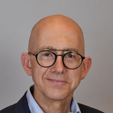 Smiling bald man wearing round glasses and a suit jacket.