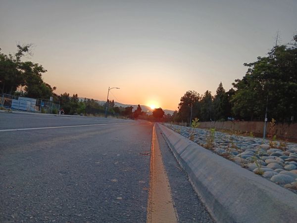 Sun setting over an empty road lined with trees and rocks.