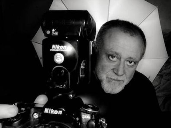 Black and white portrait of a man with a Nikon camera and umbrella lighting.