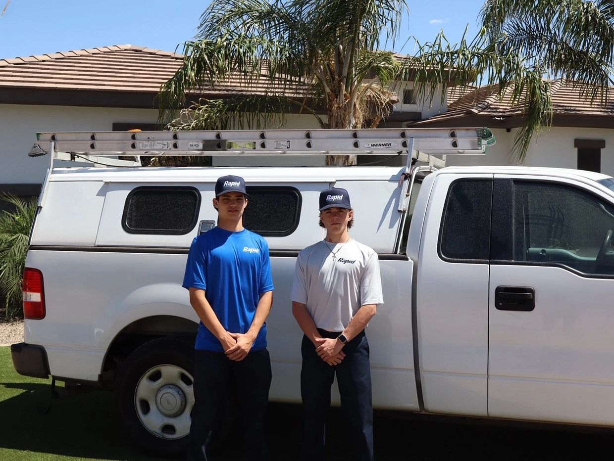 Two young men in 'Rapid' uniforms stand by a white work truck with a ladder on top.