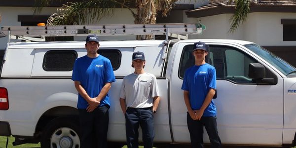 Three workers stand by a white utility truck with ladders on top.