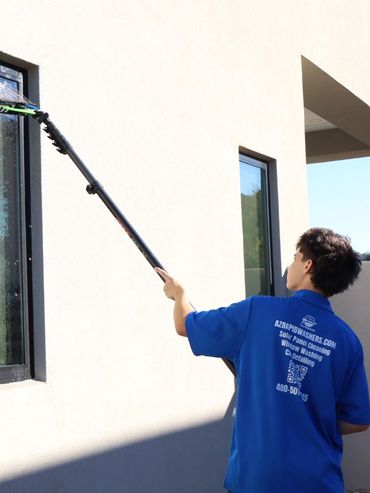 Person cleaning an outdoor window with a long-handled tool.