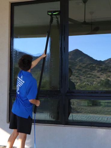 Person cleaning large windows with an extendable tool outside a house.