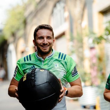 Smiling man holding a black medicine ball outdoors.