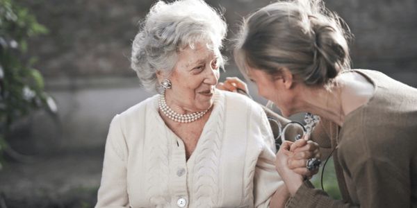 An elderly woman and a younger woman share a joyful moment outdoors.