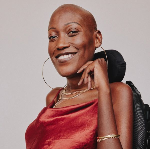 Confident woman smiling warmly, wearing a red dress and hoop earrings.