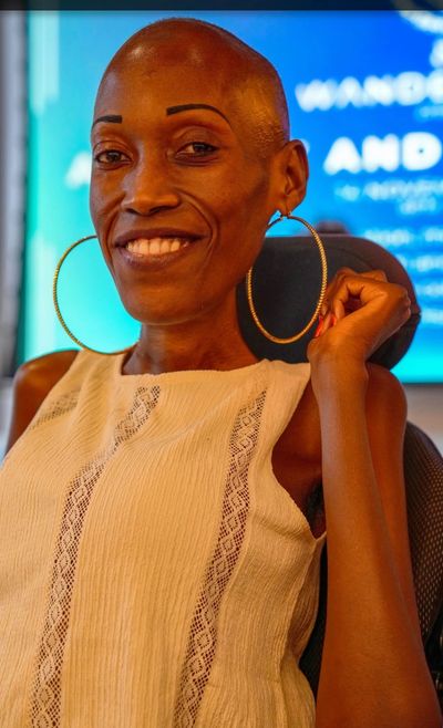 Beautiful bald headed Black woman who is smiling brightly as she sits in a motorized wheelchair. 