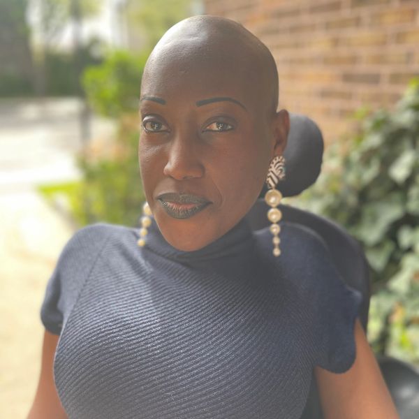 Confident woman with bold earrings and dark lipstick in natural light.