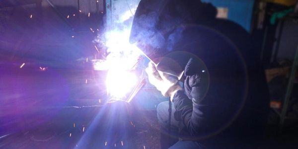 A person welding metal, wearing protective gloves and a helmet.