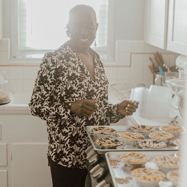 Betty smiling with homemade bakery items: blueberry, cherry, peach, and caramel apple pies