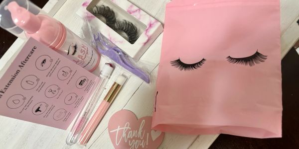 Eyelash extension kit with tools and accessories in pink packaging.