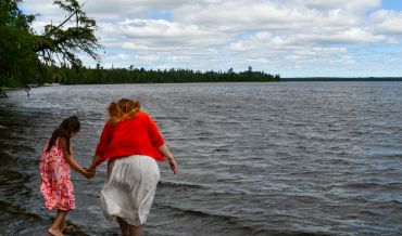Two girls holding hands by the shore.