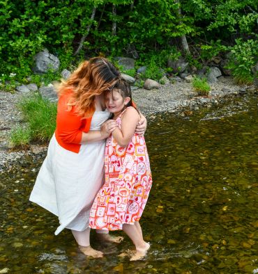 A mother and daughter hug joyfully in shallow water.
