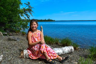 Girl sitting on a log by a lake on a sunny day.