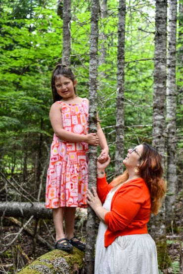 Woman looking up at a girl holding a tree branch in a forest.