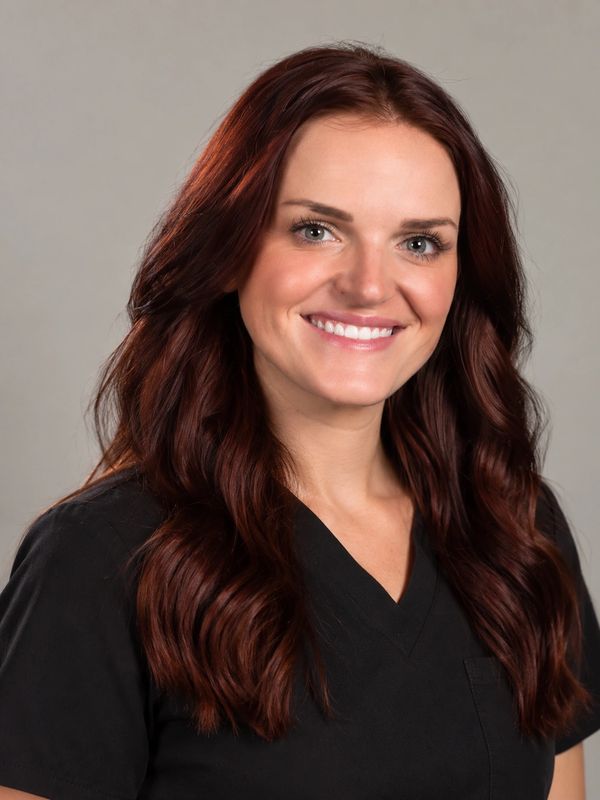 Smiling woman with long brunette hair in black medical scrubs.
