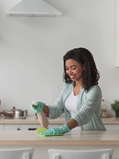 A woman with gloves using a spray bottle wipes down the counter with a cloth.