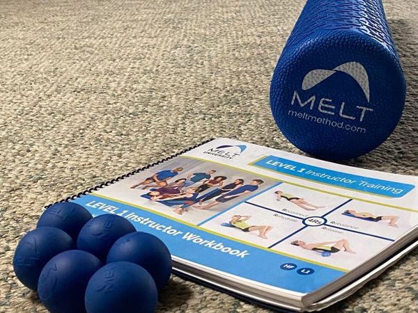 MELT Method workout tools and Level 1 Instructor Training workbook on carpet.