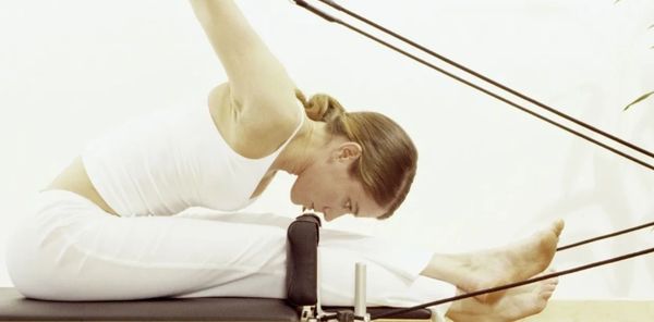 Woman stretching forward in a Pilates exercise using resistance bands.
