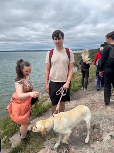 Group of people with a dog by a lakeside path on a cloudy day.