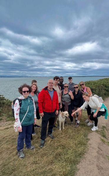 Group of friends with a dog by the waterfront under cloudy skies.