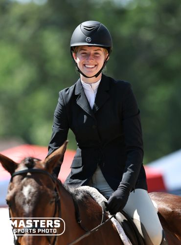 Smiling equestrian riding a horse in competition attire.