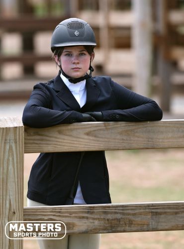 Young equestrian with helmet leaning on a wooden fence.