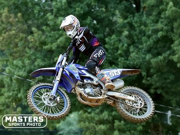 Motocross rider airborne on blue dirt bike in forest setting.