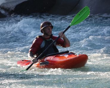 A man kayaking on whitewater rapids with a green paddle.