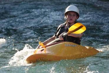 A young person kayaking in turbulent water wearing a helmet.